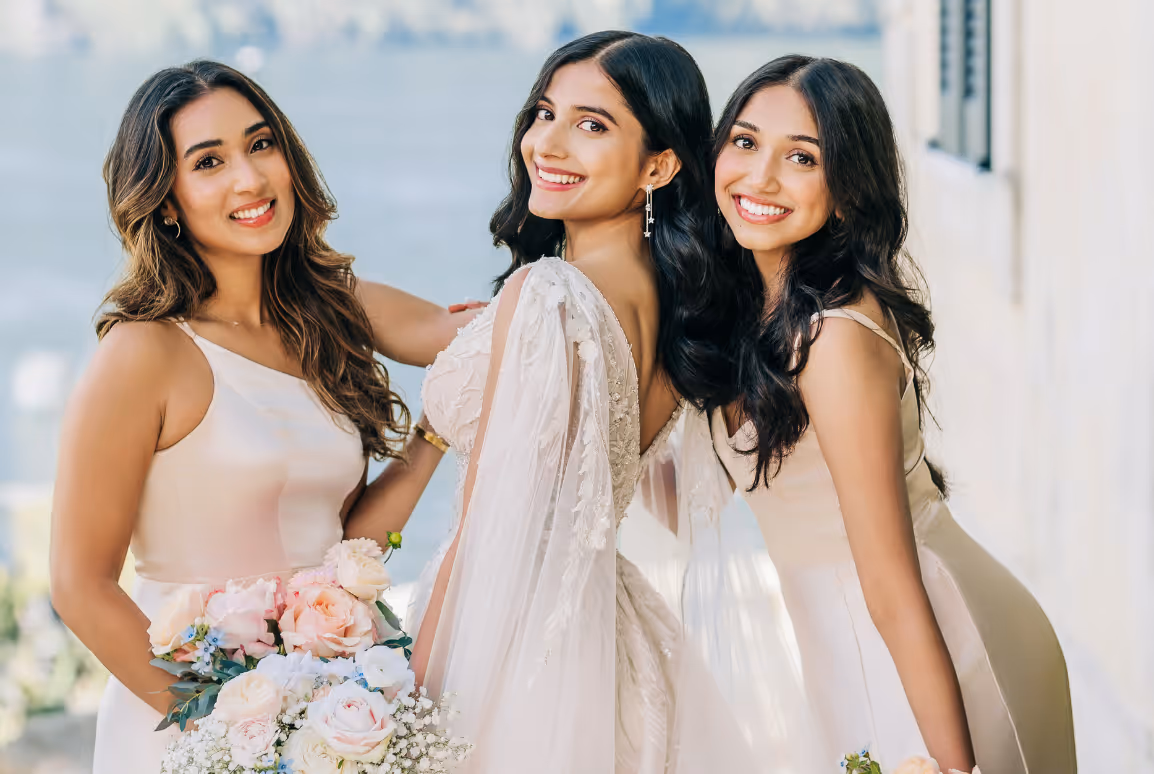 A portrait of the bride, smiling with two bridesmaids in satin champagne-toned dresses during a destination wedding at Villa Cipressi.
