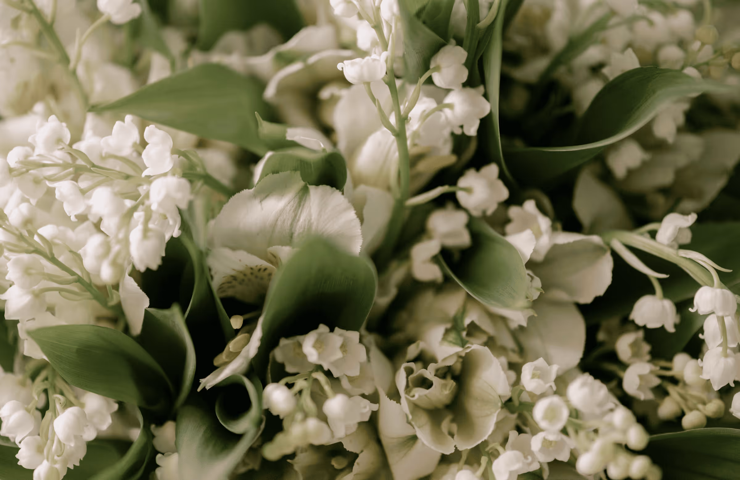 A close-up macro photograph of a luxury wedding bridal bouquet featuring delicate white lily of the valley flowers and fresh green leaves at Castello Durini.