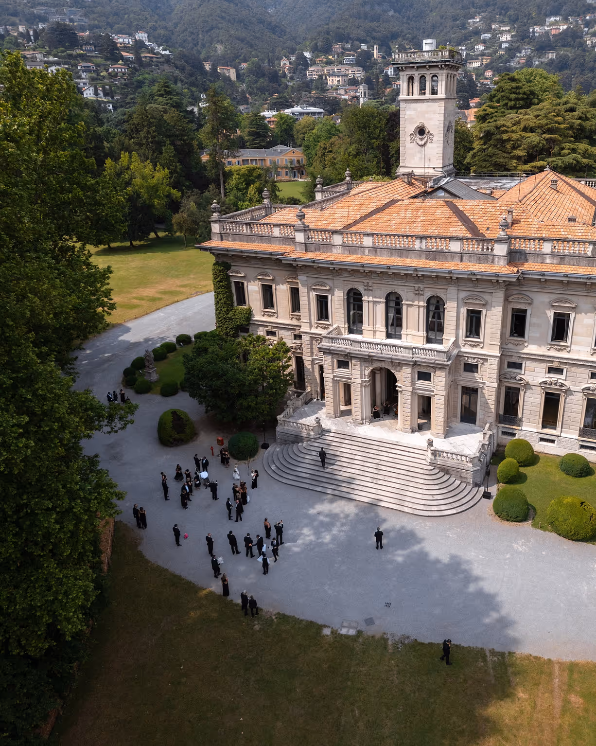 Veduta aerea dall'alto della storica e monumentale Villa Erba sul Lago di Como, con gli ospiti del matrimonio che si radunano nel piazzale esterno circondato dal parco.