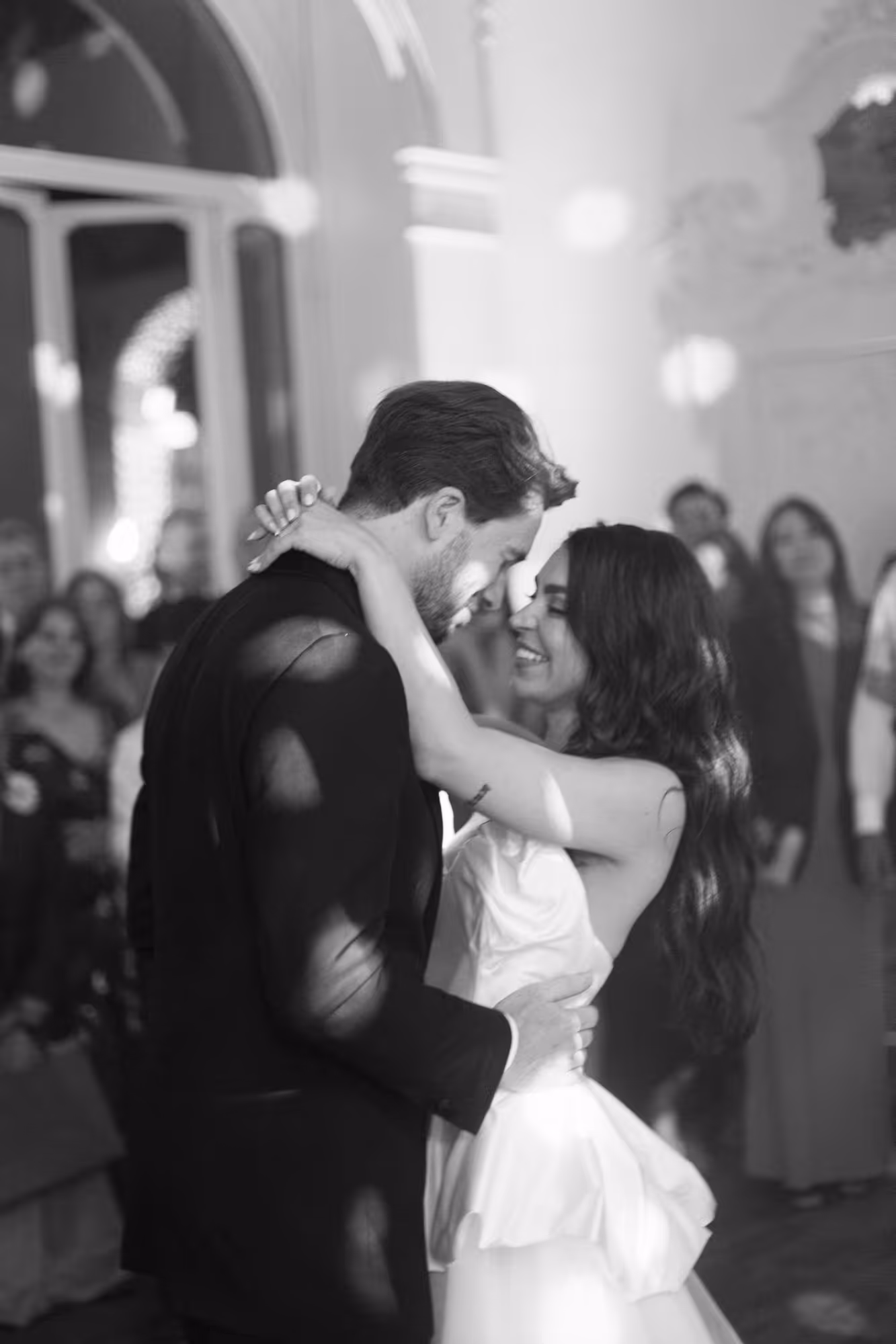 A vertical black and white wedding photograph highlighting an emotional first dance, with the bride holding her husband closely and smiling radiantly during their party at Villa Grumello.