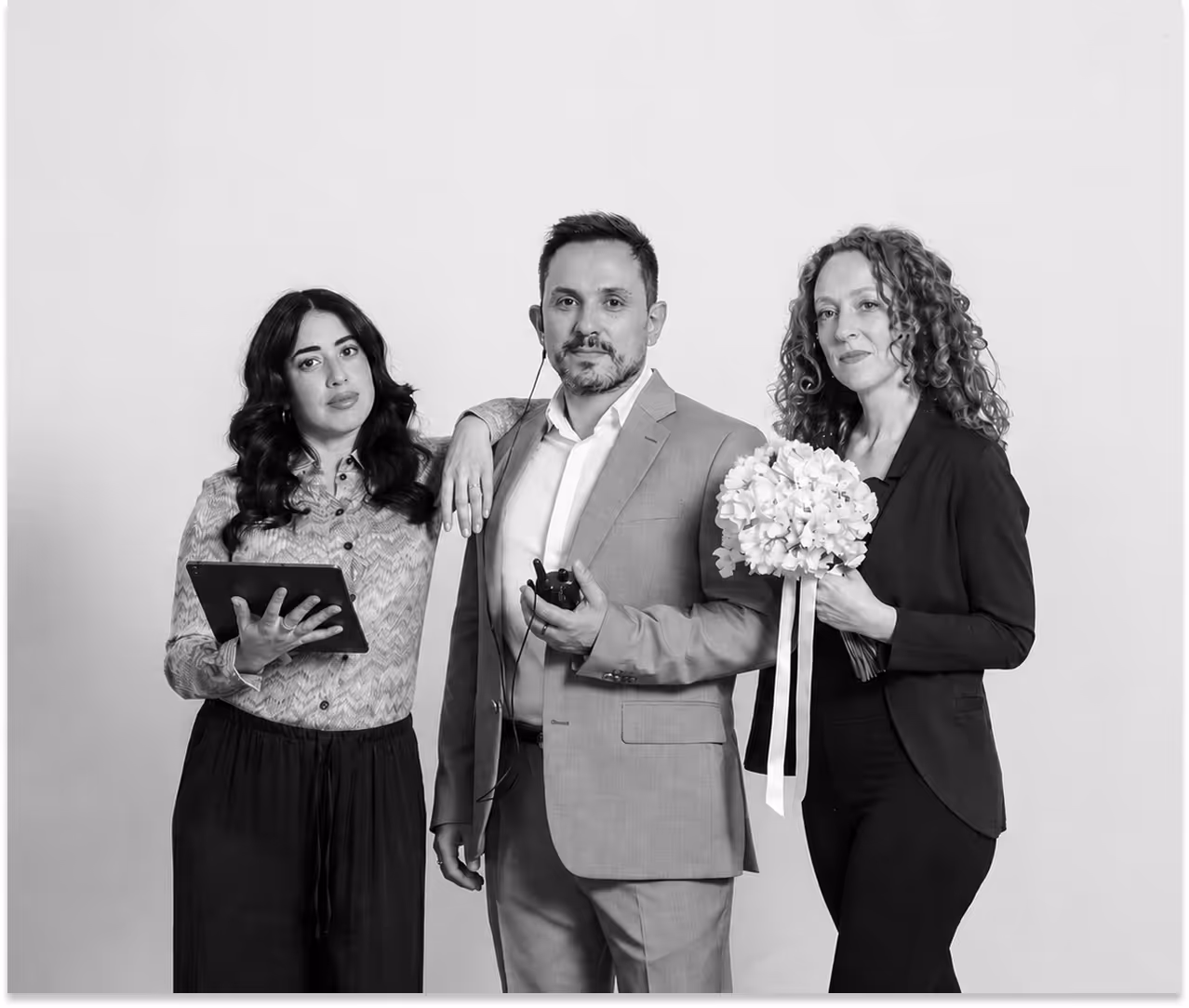 Foto in bianco e nero del team di wedding planner de Il Bosco degli Eventi: Melissa con un tablet, Omar al centro in giacca e Danila con un bouquet di rose bianche.