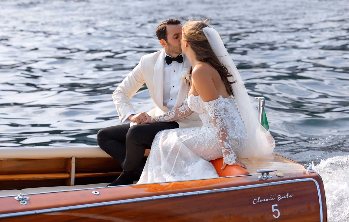 Una coppia di sposi eleganti si scambia un bacio romantico a bordo di un motoscafo d'epoca in legno, durante un matrimonio di lusso sul Lago di Como a Villa Erba.