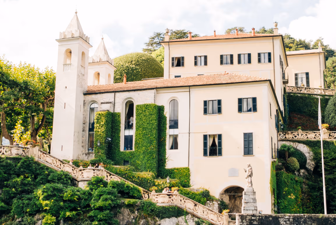 A beautiful daylight photograph showcasing the grand architecture, ivy-covered stone walls, and historic church towers of Villa del Balbianello wedding venue on Lake Como.