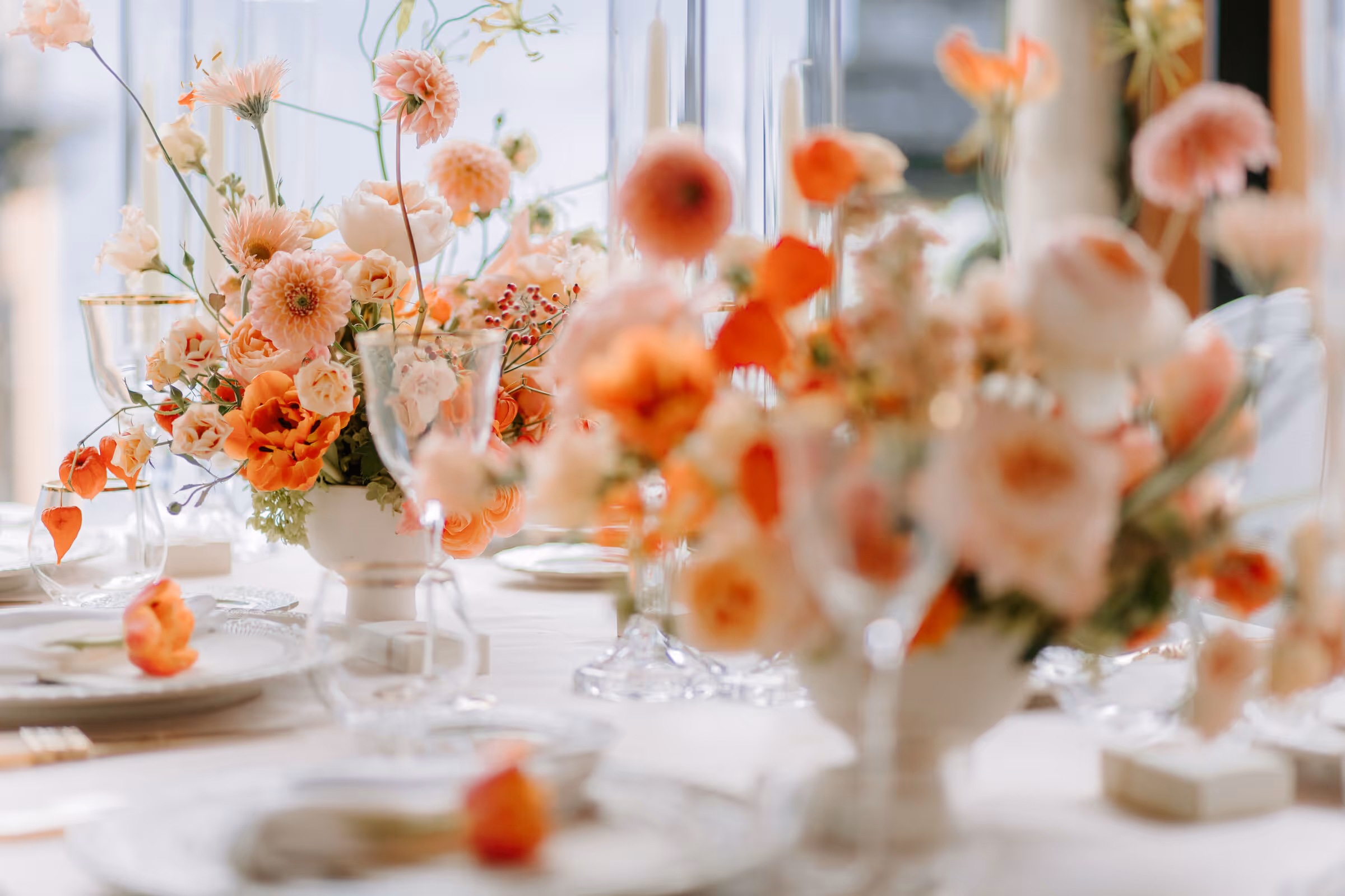 A close-up wedding reception tablescape photograph at Villa La Cassinella showing a lush floral centerpiece filled with peach roses, pink dahlias, and coral flowers alongside elegant crystal glassware.