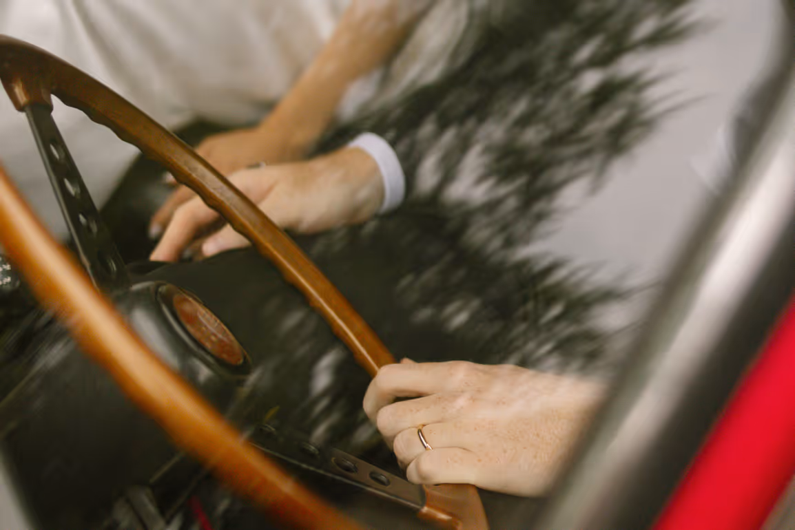 An artistic, motion-blurred close-up shot of a groom's hand wearing a gold wedding band on a classic wooden steering wheel of a vintage getaway car at Villa Grumello.